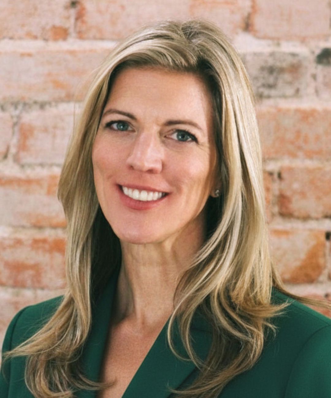 Smiling woman in a green blazer in front of a brick wall