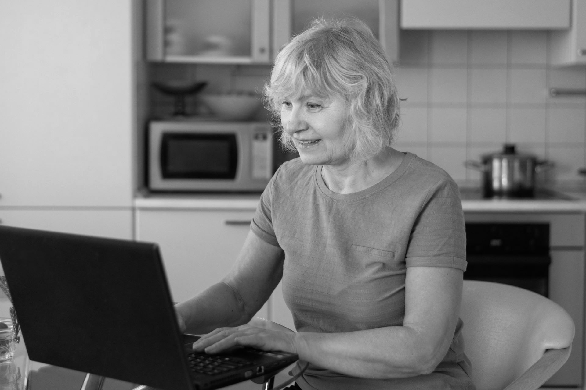 elderly woman at laptop in kitchen, black and white photo