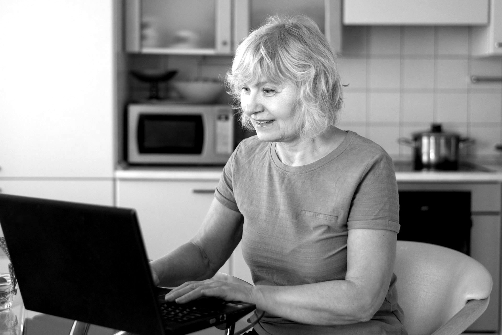 elderly woman at laptop in kitchen, black and white photo