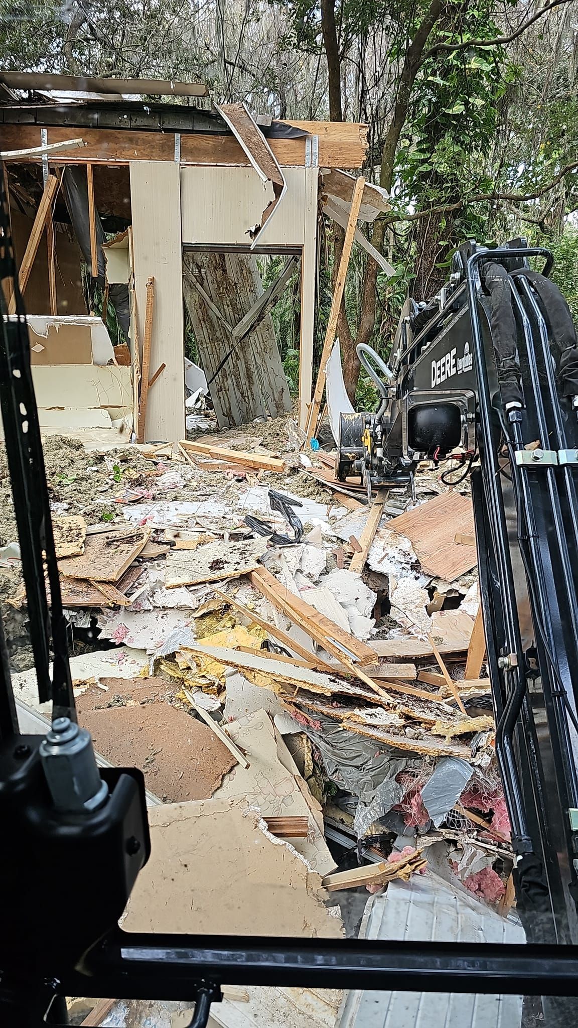 View from the cab of heavy machinery overlooking the site of a building being demolished, surrounded by rubble and trees.