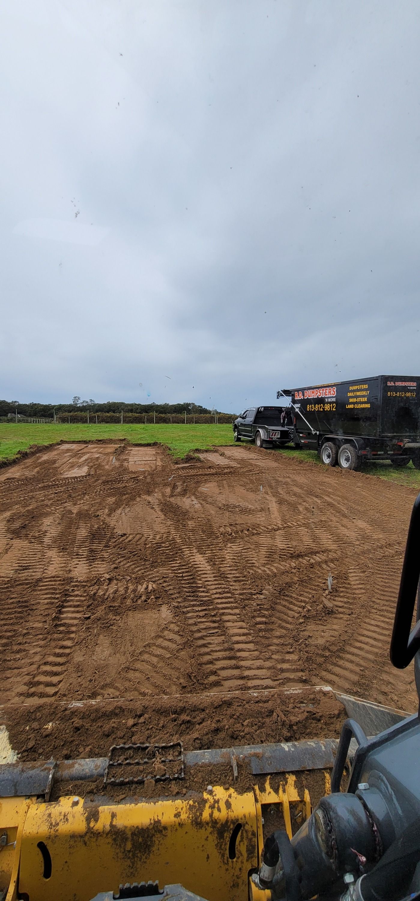 View from the cab of a yellow construction vehicle overlooking a muddy field with a truck parked in the distance.