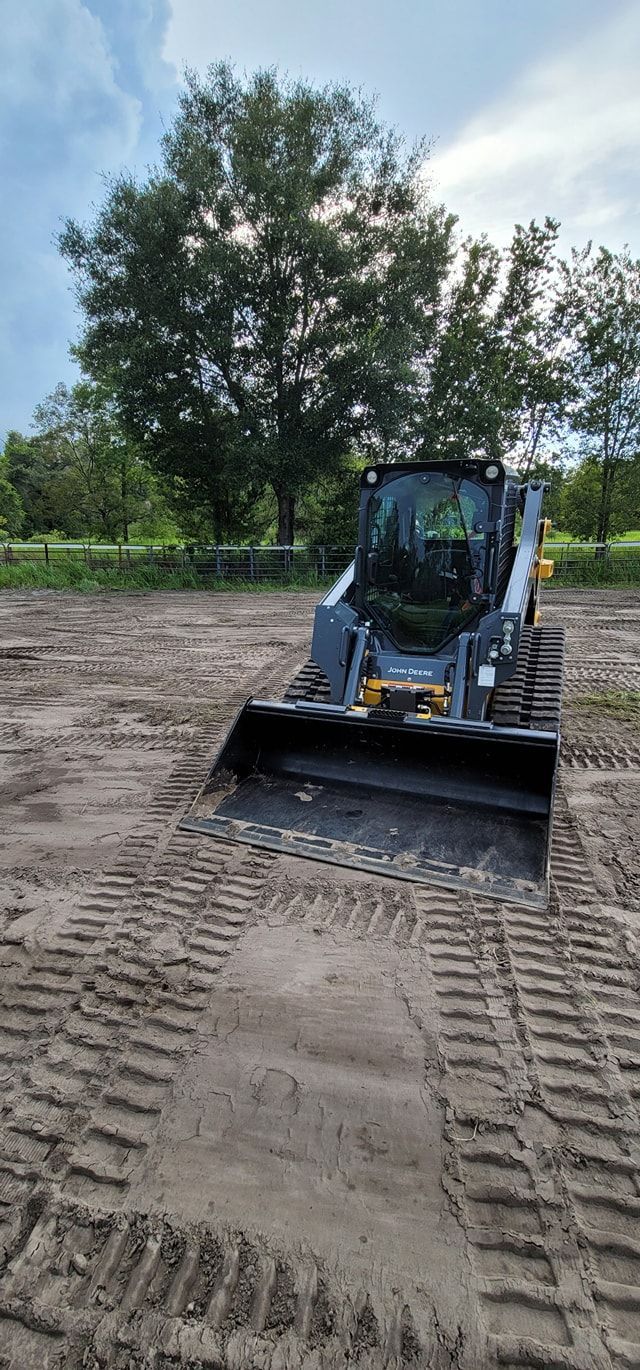 A gray skid steer loader with tracks sits in a field of dirt under a cloudy sky.