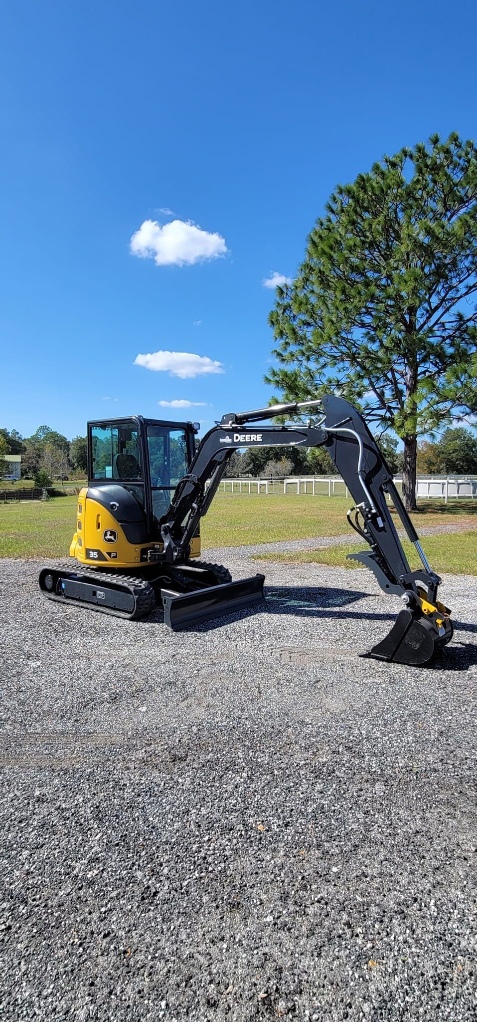 A yellow and black Caterpillar mini excavator parked on a gravel surface under a clear blue sky.