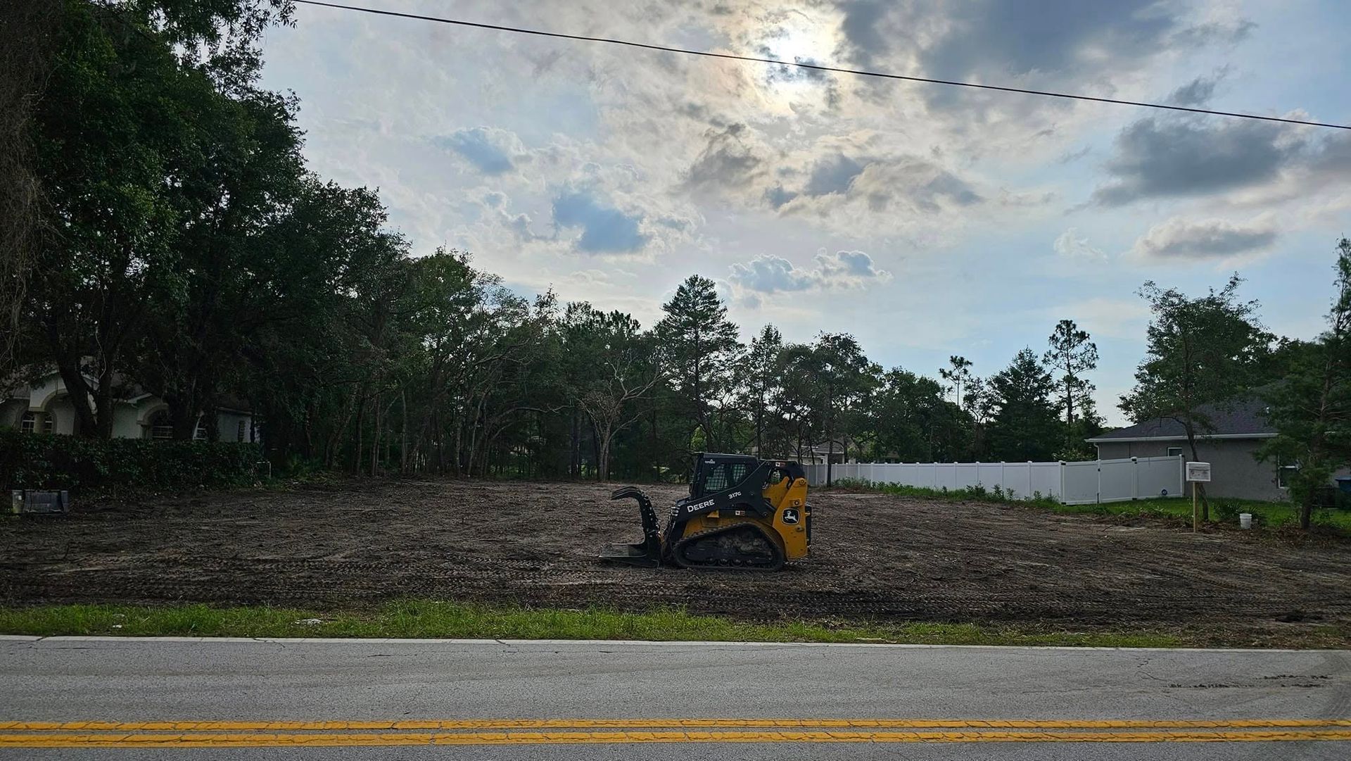 A small yellow construction vehicle sits in the middle of a cleared, dirt-covered vacant lot under a cloudy sky.