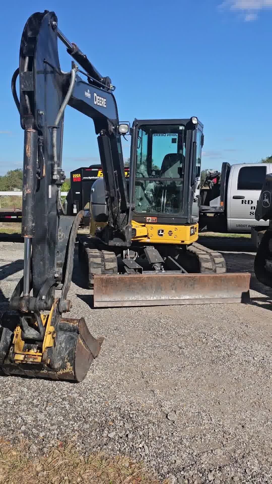 A yellow and black excavator parked on a gravel lot under a clear blue sky, next to a white pickup truck.