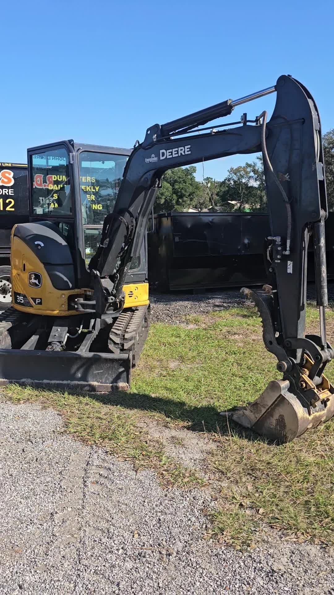 A yellow and black John Deere mini excavator parked on a grassy lot under a clear blue sky.