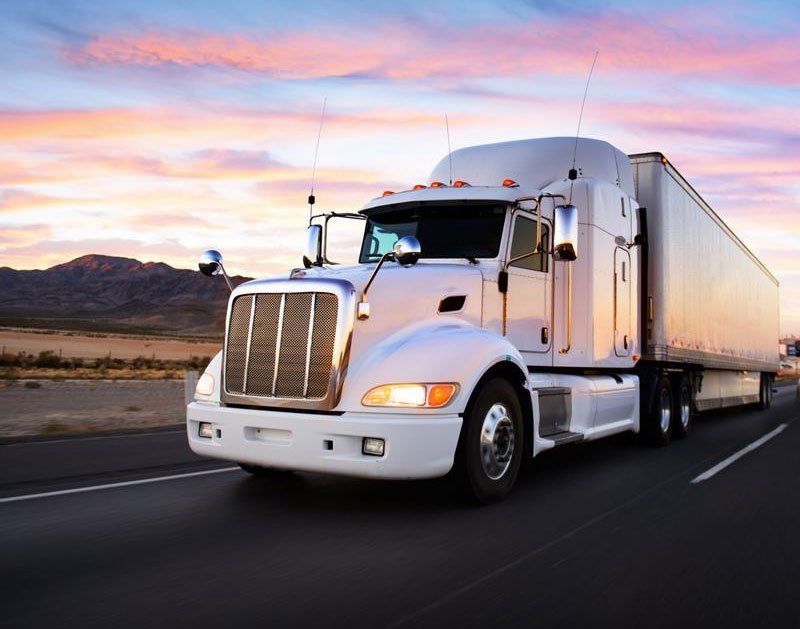 White semi-truck driving on a highway at sunset.