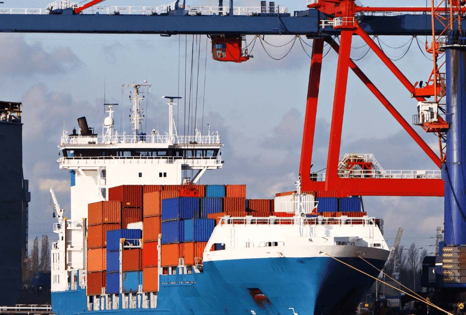Cargo ship at port, being loaded/unloaded by a large red and blue crane. Sunny day.