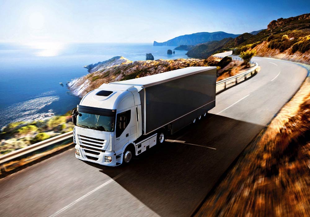 White semi-truck drives on a coastal highway, ocean visible in the background.