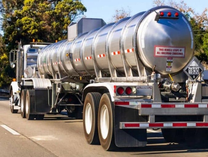 Tanker truck transporting liquid on a road, silver tank, white cab, red and white safety markings.