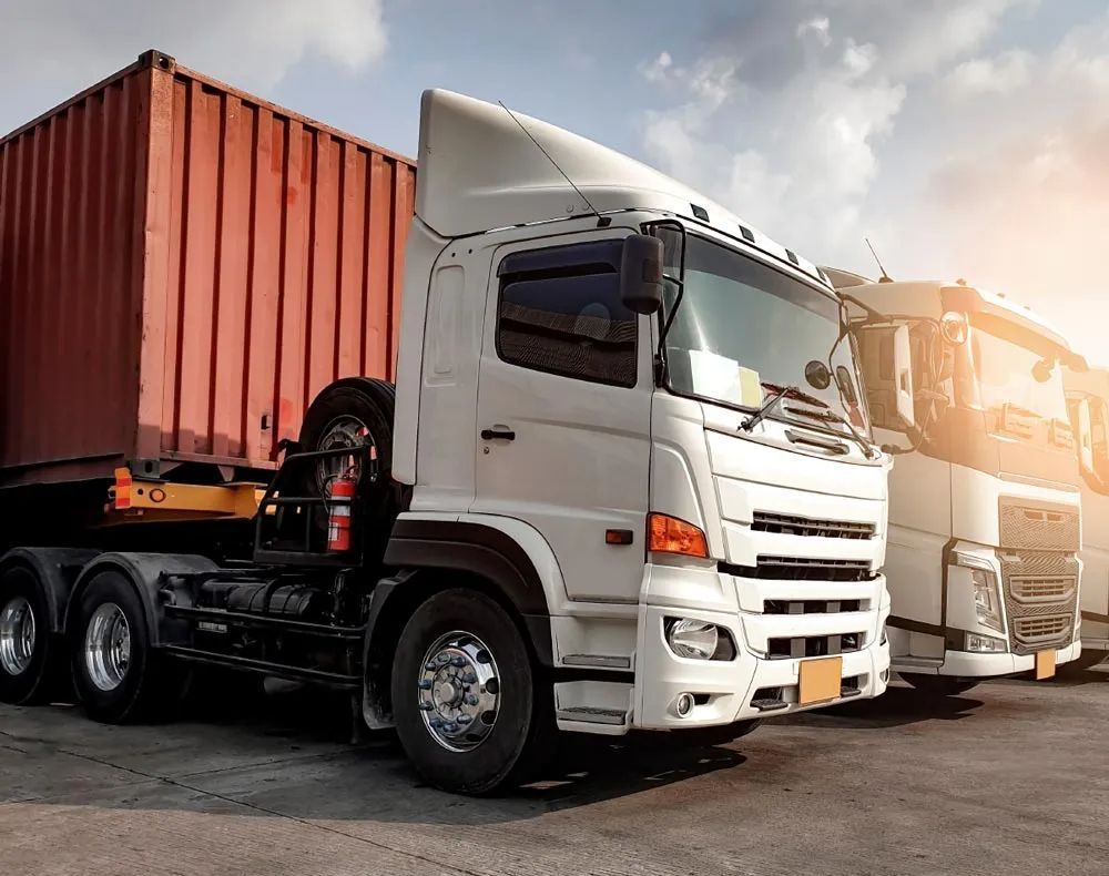 White semi-truck carrying a red cargo container, parked outdoors, sunlight.