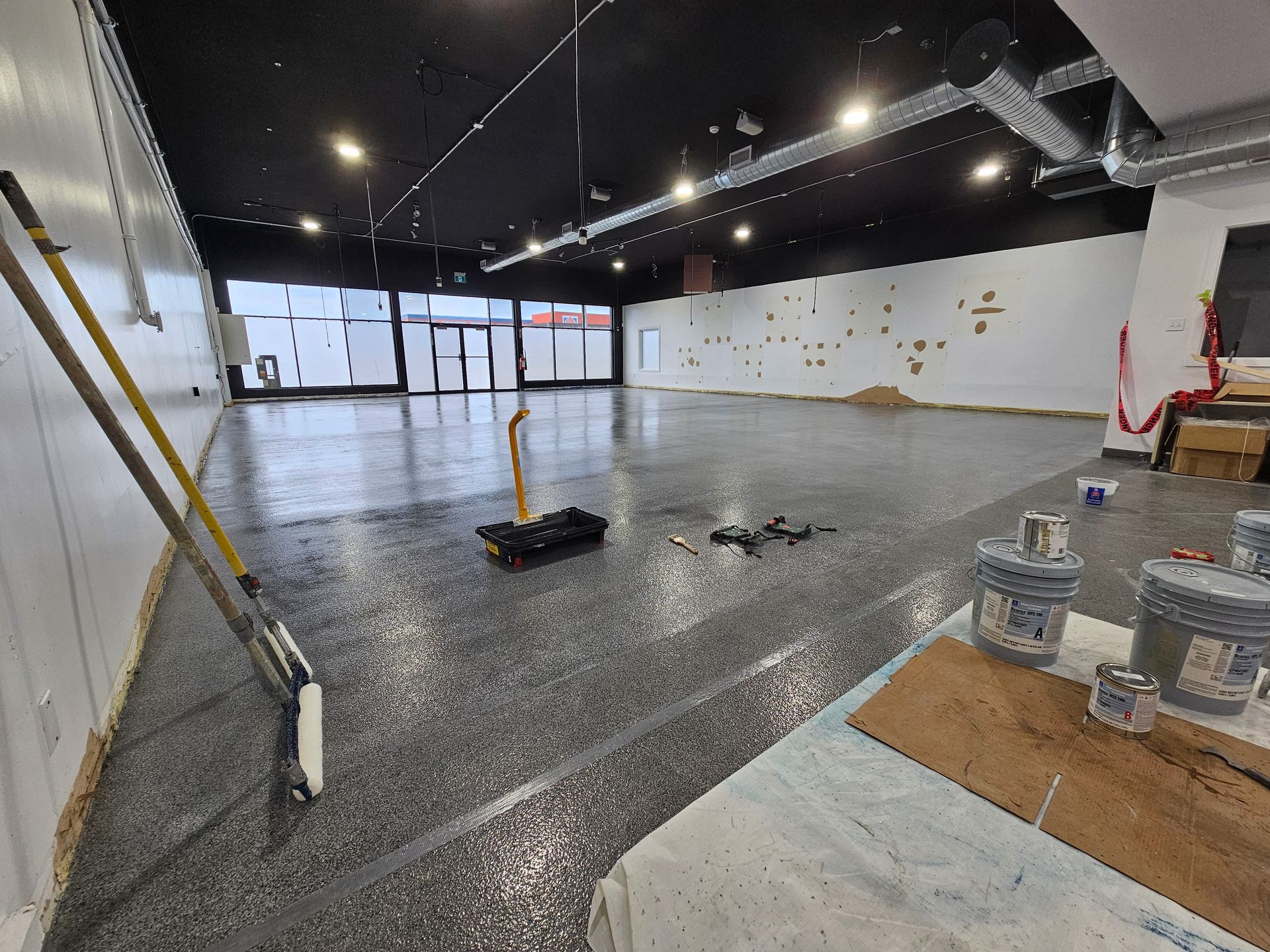 Espace commercial vide avec sol époxy, outils de construction et seaux de peinture.