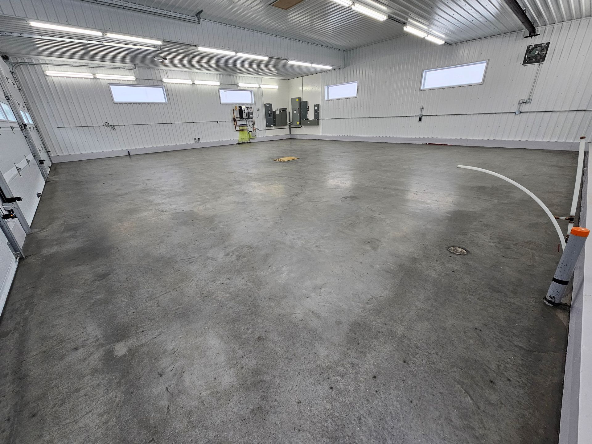 Un espace intérieur vide en béton, avec une ligne blanche incurvée, entouré de murs blancs, de portes et de lumières.