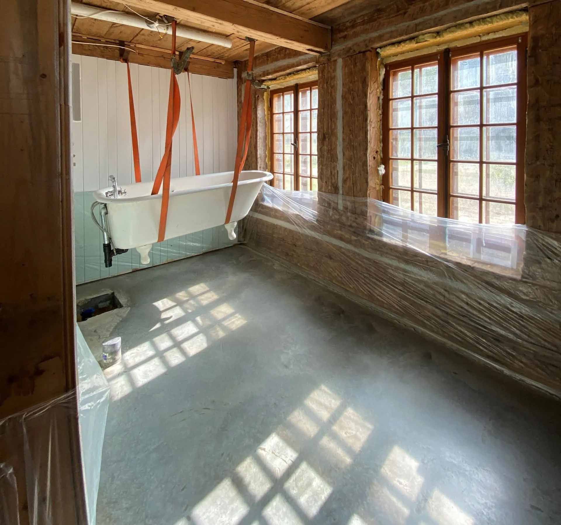 Salle de bain en cours de rénovation. Plafond et poutres apparentes, baignoire, fenêtres, film plastique.
