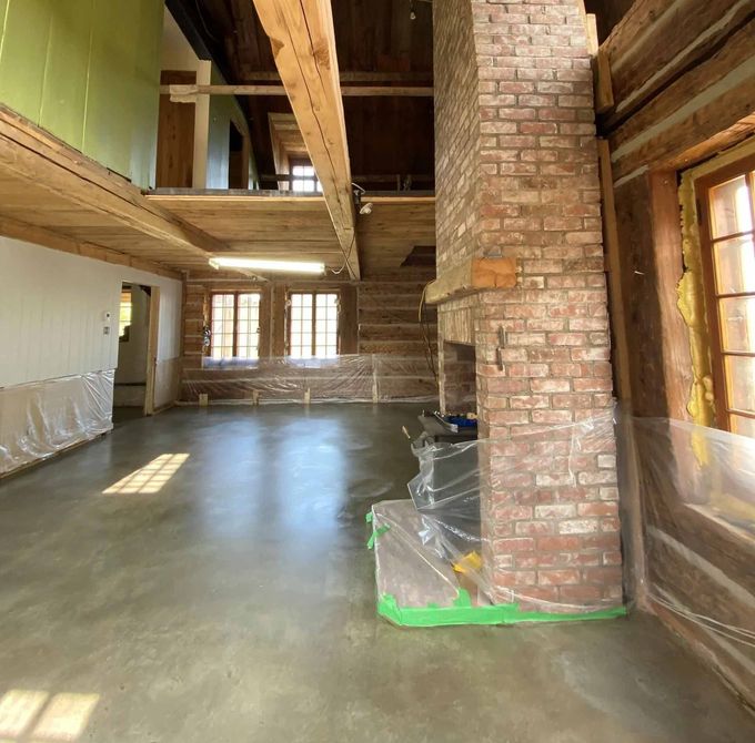 Intérieur d'une pièce rustique avec poutres apparentes, cheminée en briques et sol en béton.