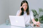 Woman in a white t-shirt on a phone call, using a laptop and tablet with a stylus.