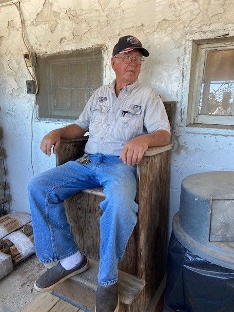 A man is sitting on a wooden chair in front of a window.