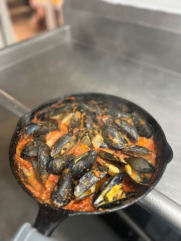 A pan filled with mussels and tomato sauce on a counter.