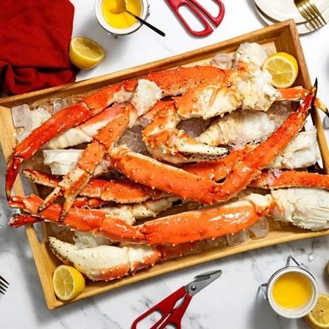 A wooden tray filled with crab legs and lemons on ice.