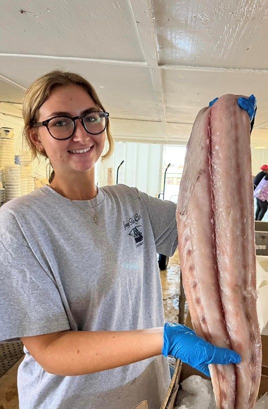 A woman wearing glasses and blue gloves is holding a large piece of fish.