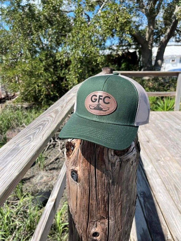 A green and white trucker hat is sitting on top of a wooden post.