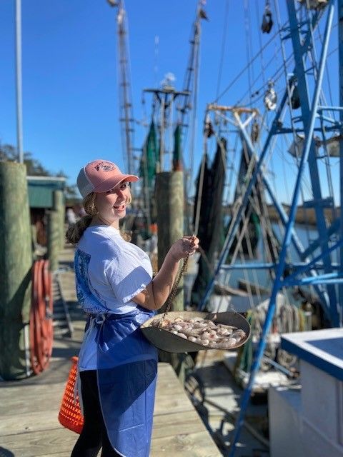 A woman is holding a tray of shrimp on a dock.