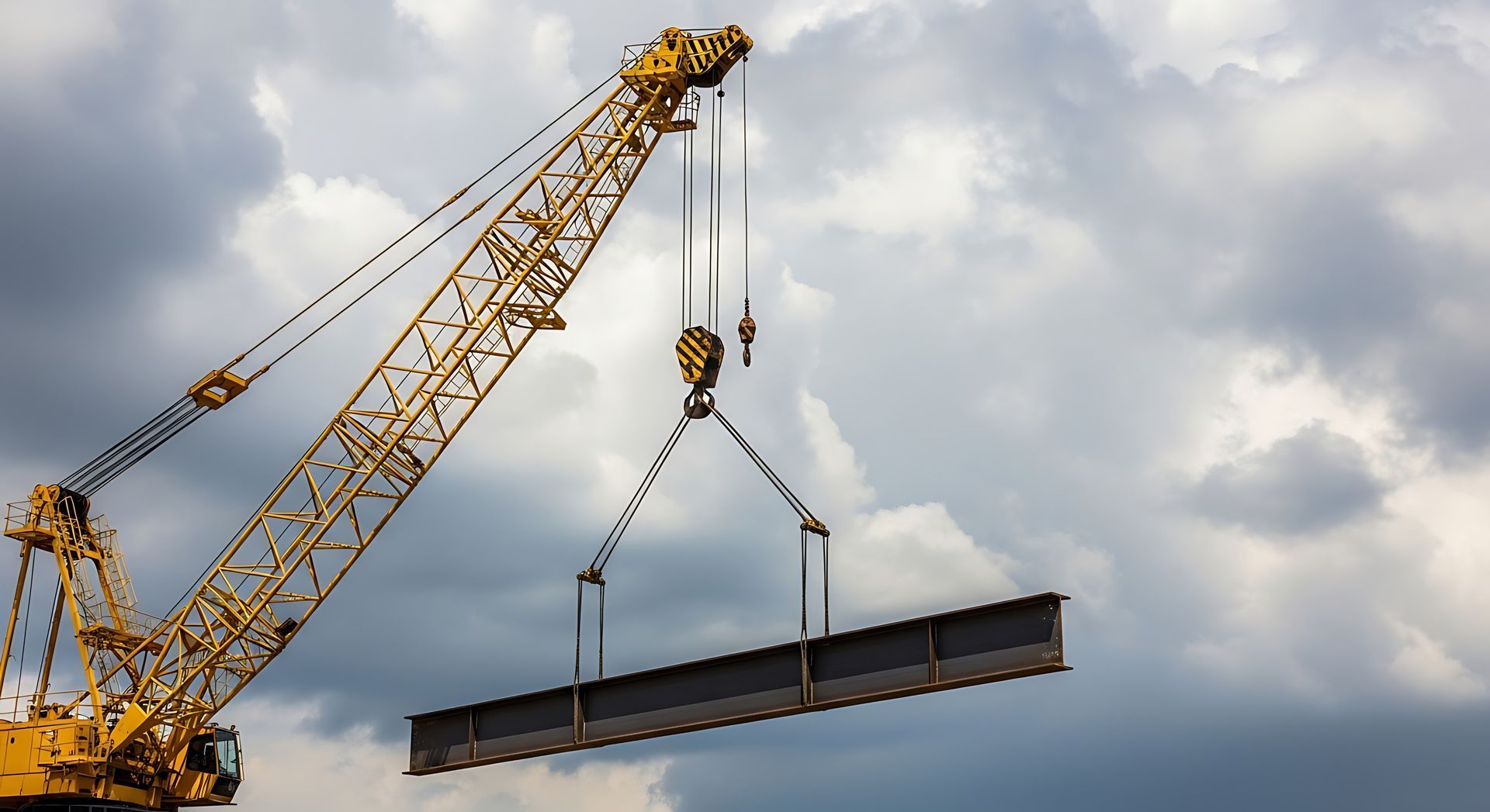 Yellow crane lifting a long steel beam against a cloudy sky