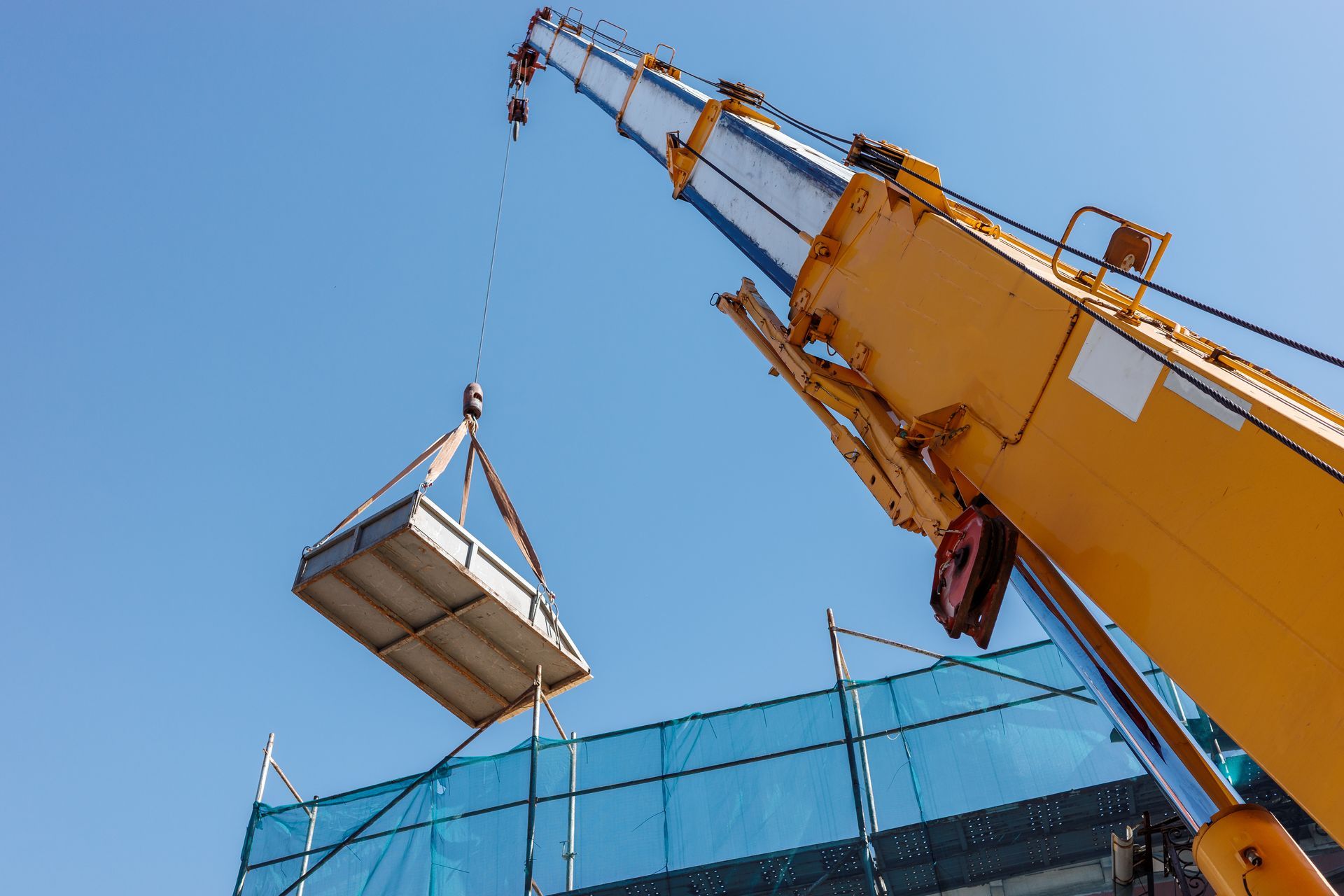 Mobile crane hoisting a rigged metal load with slings during a rigging operation.