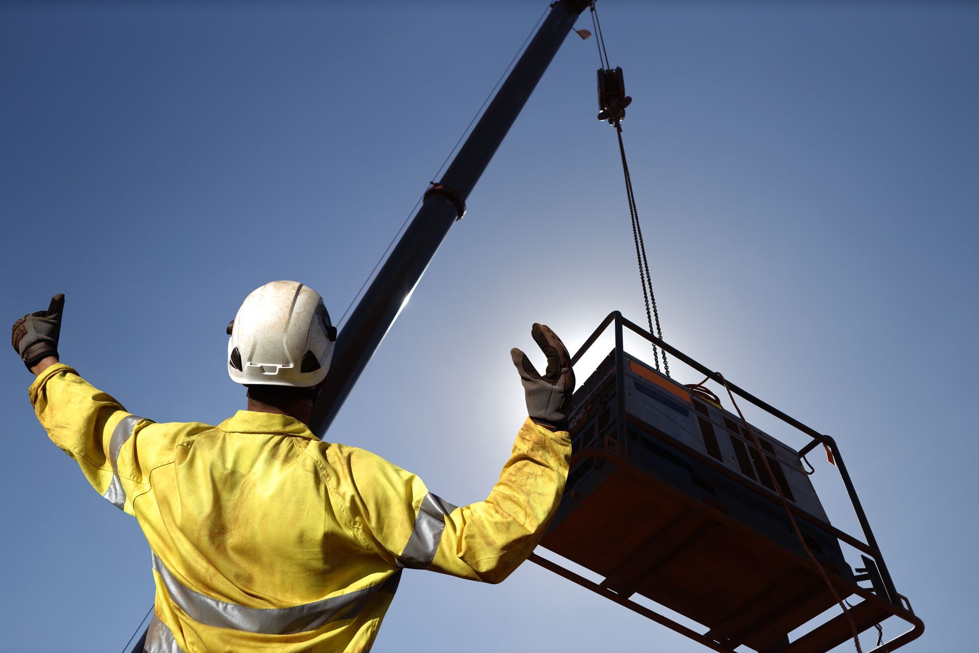 Crane rigger signaling a suspended crane load using specialized rigging hardware during an industrial lift. Crane rigger signaling a suspended crane load using specialized rigging hardware during an industrial lift.