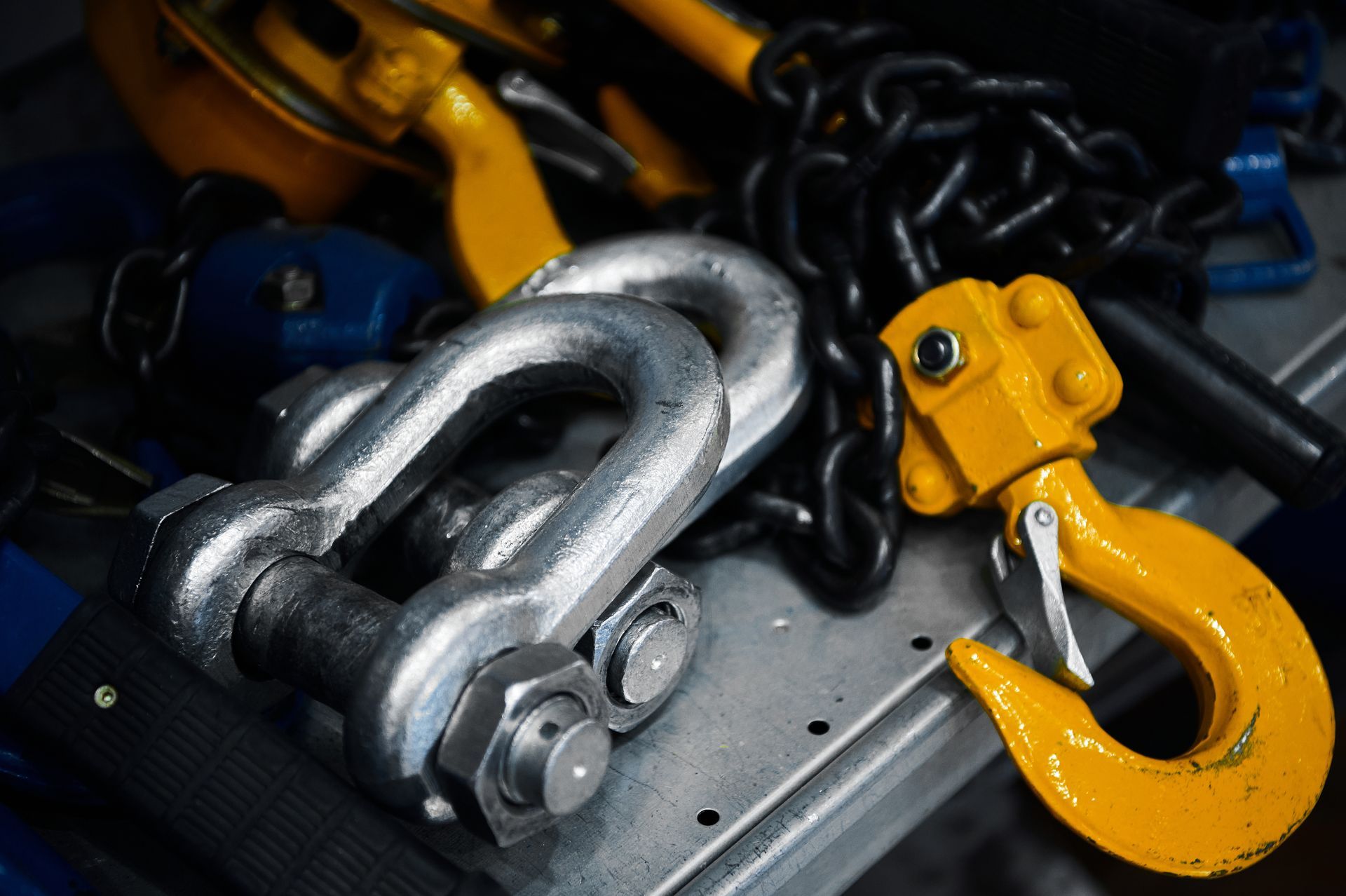 Steel shackles, chain, and a yellow rigging hook on a metal surface.