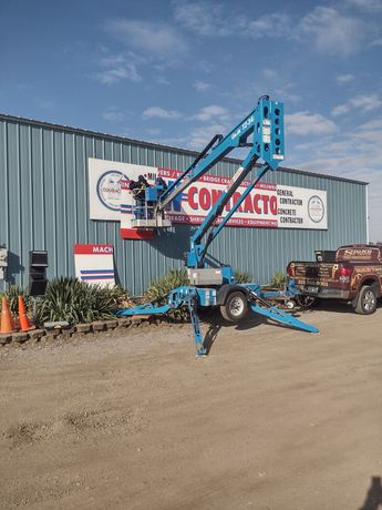 Blue boom lift parked outside a building with a sign, on a gravel lot under a blue sky.