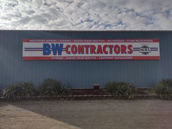 B&W Contractors sign on a gray building, with shrubs and a dirt foreground.