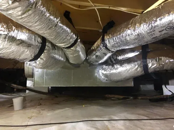 HVAC ductwork and air handler unit in a crawlspace, with insulated flexible ducts and metal components.
