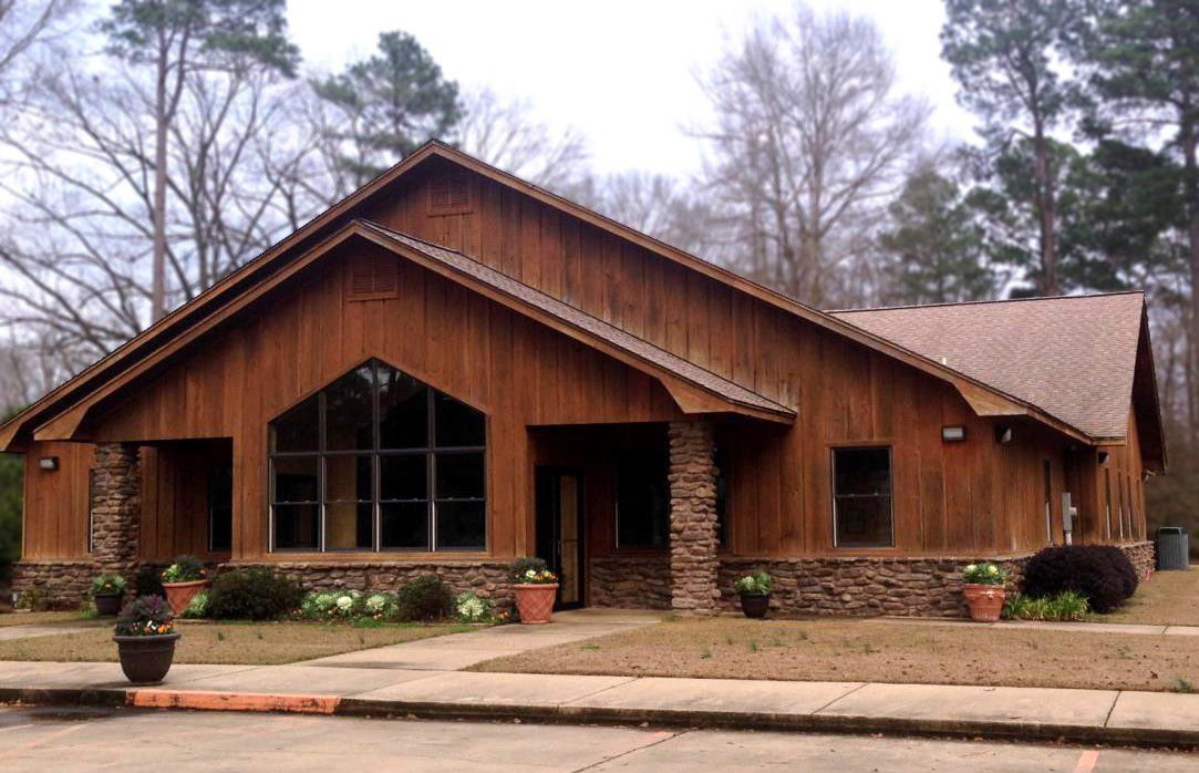 Wooden lodge with stone base and large windows, set among bare trees along a quiet street