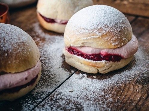 Three sandwiches with powdered sugar on top are on a wooden table.