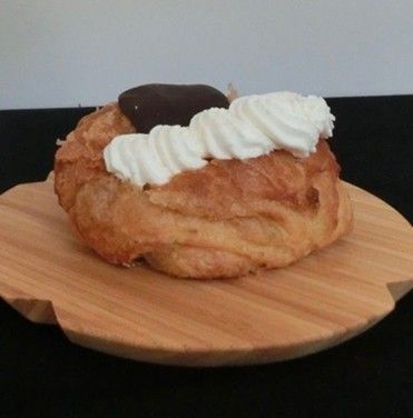 A pastry with whipped cream and chocolate on a wooden cutting board