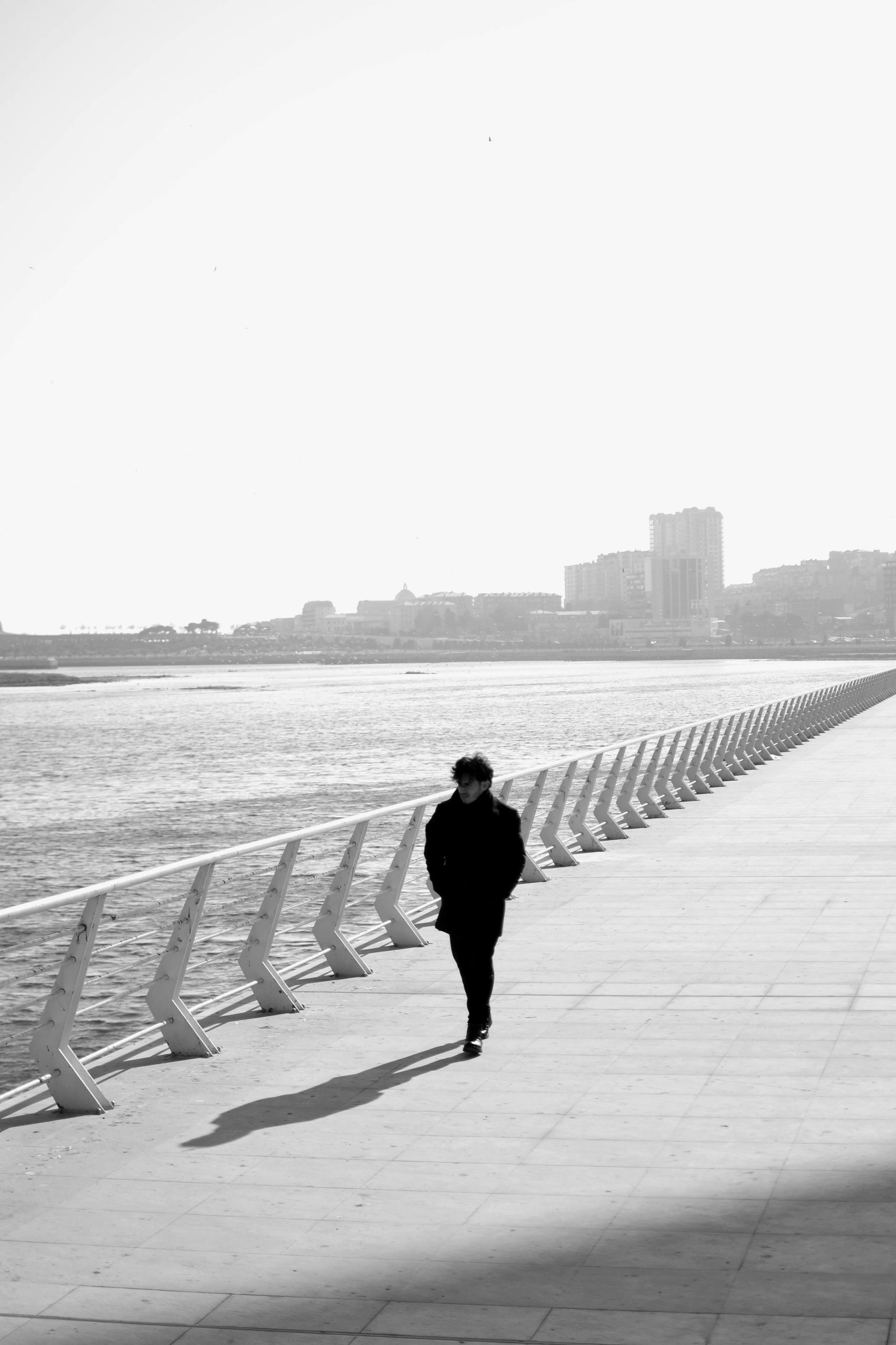 A man is walking down a sidewalk next to a body of water.