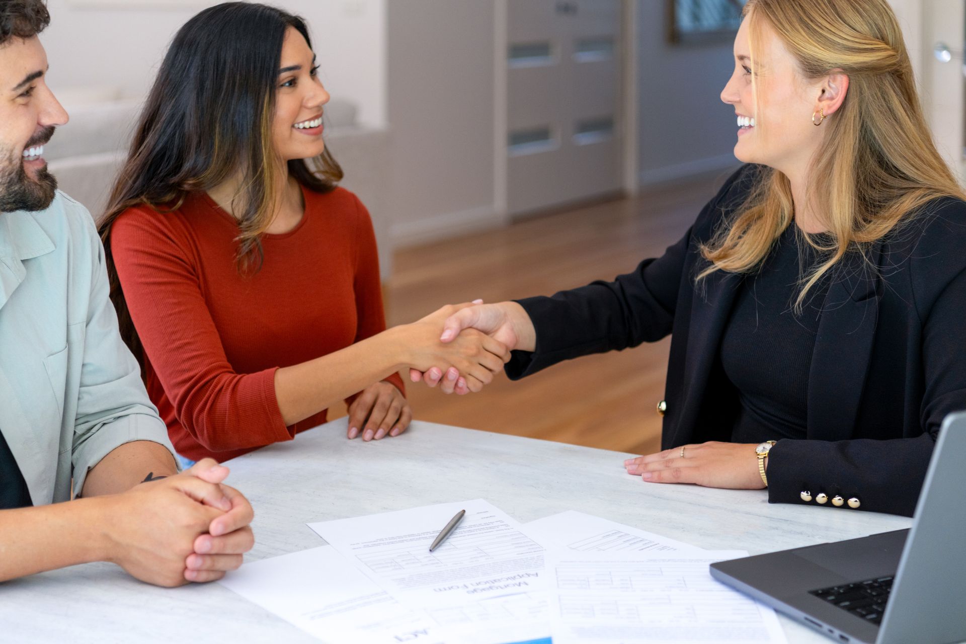 Two women shake hands during a business meeting discussing auto insurance agency services.