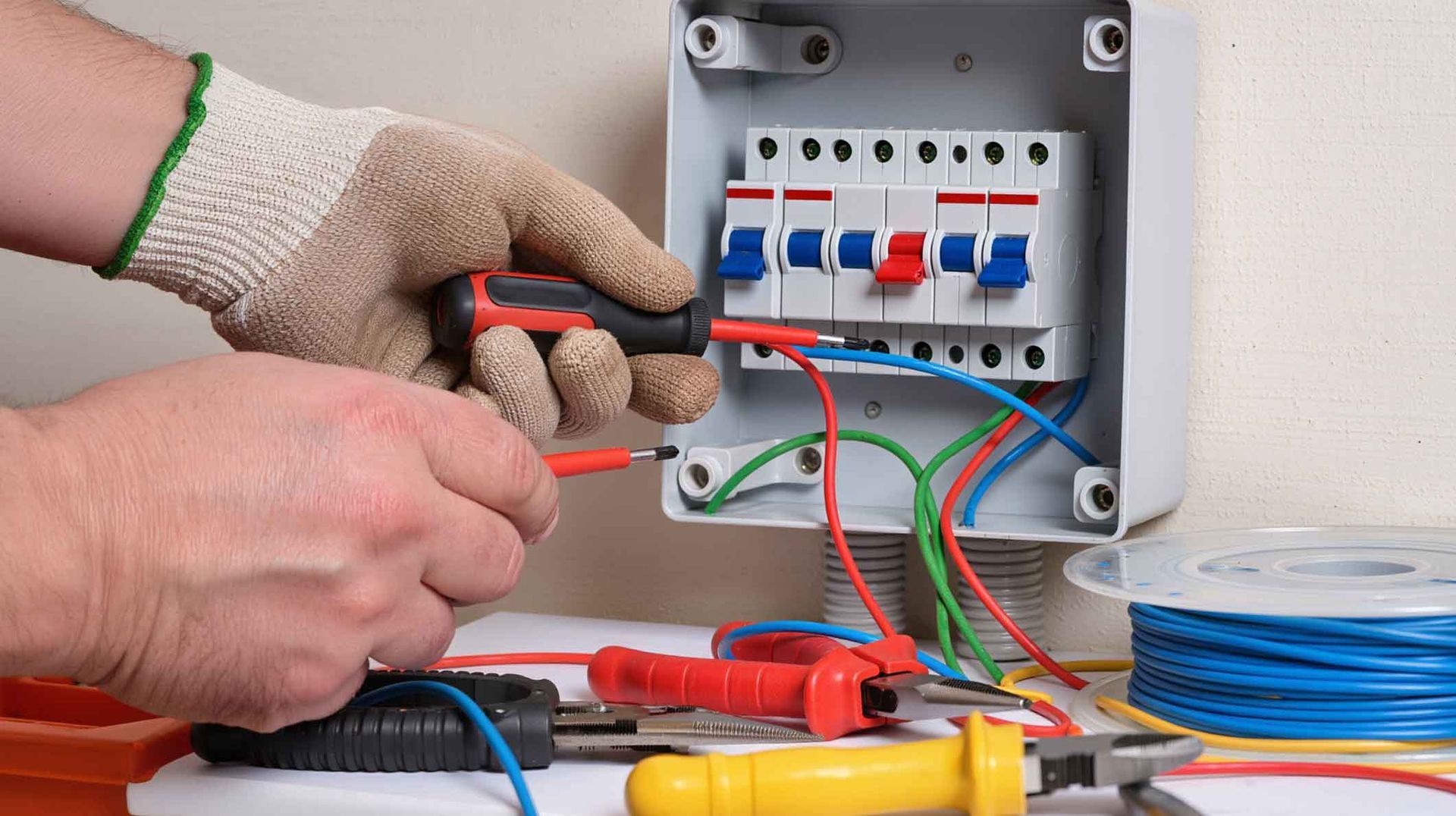 Gloved hands wiring a small electrical panel with circuit breakers and colorful cables Gloved hands wiring a small electrical panel with circuit breakers and colorful cables