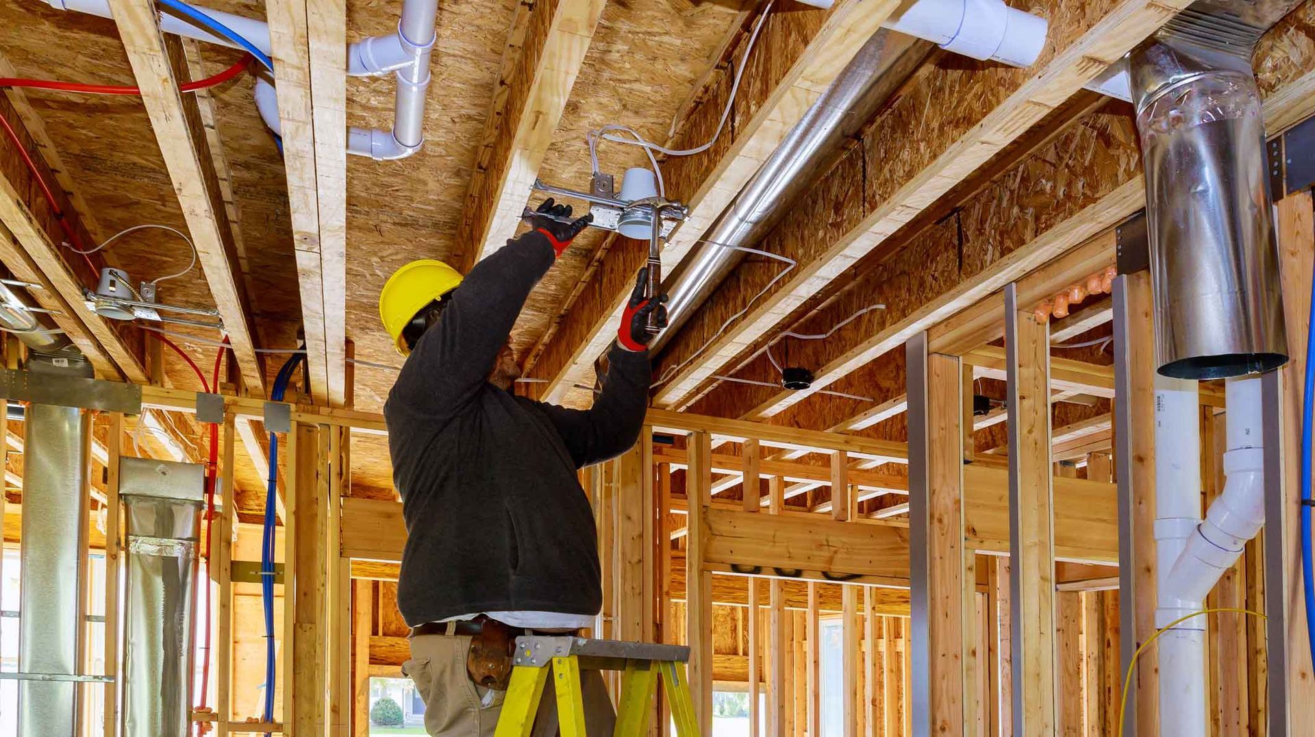 Worker fastening pipes in a framed house under construction, wearing a hard hat and safety vest Worker fastening pipes in a framed house under construction, wearing a hard hat and safety vest
