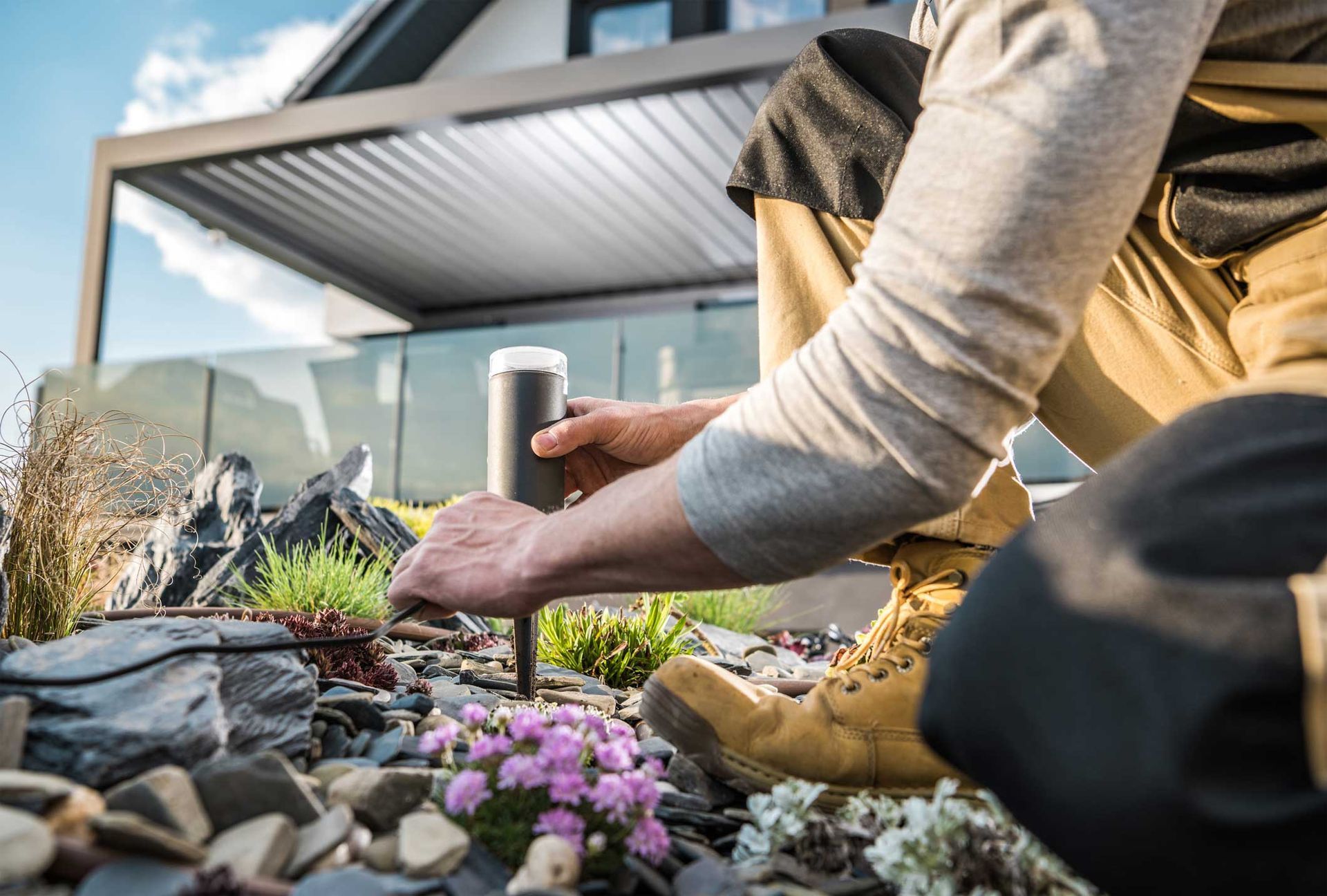 Person planting flowers in a raised garden bed beside a house patio Person planting flowers in a raised garden bed beside a house patio