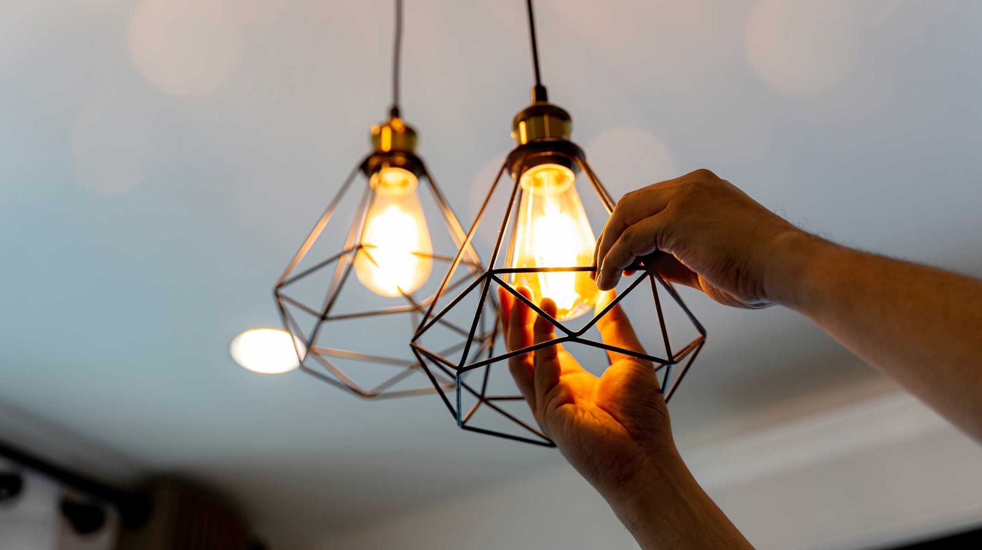 Hands adjusting two lit geometric pendant lights hanging from the ceiling. Hands adjusting two lit geometric pendant lights hanging from the ceiling.