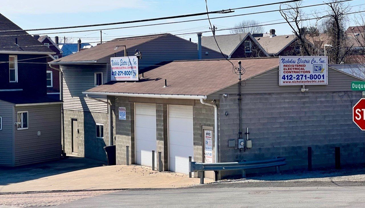 Small commercial building with garage doors and signs at a street corner, with a stop sign nearby.