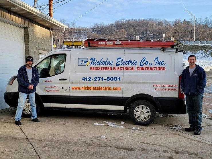 An electrical service van parked outdoors with two people standing beside it near a garage building An electrical service van parked outdoors with two people standing beside it near a garage building