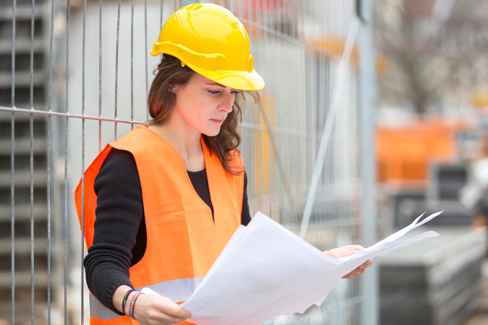 Construction worker in safety gear reviewing blueprints at active construction site. Construction worker in safety gear reviewing blueprints at active construction site.