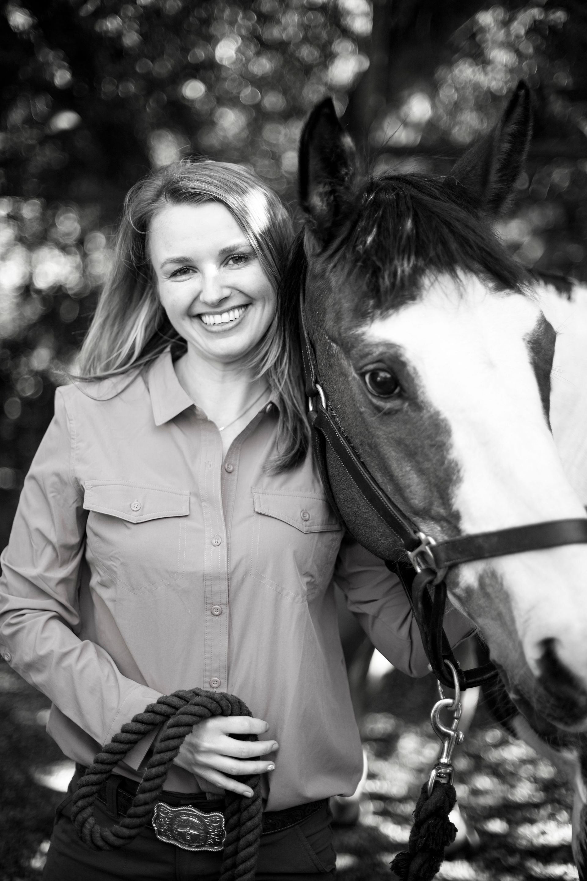 Smiling woman standing beside a horse, holding a rope halter outdoors.