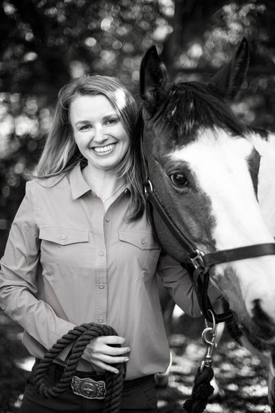 Smiling woman standing beside a horse, holding a rope halter outdoors.