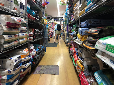 A narrow pet store aisle lined with bags of pet food, with a person walking away in the distance.