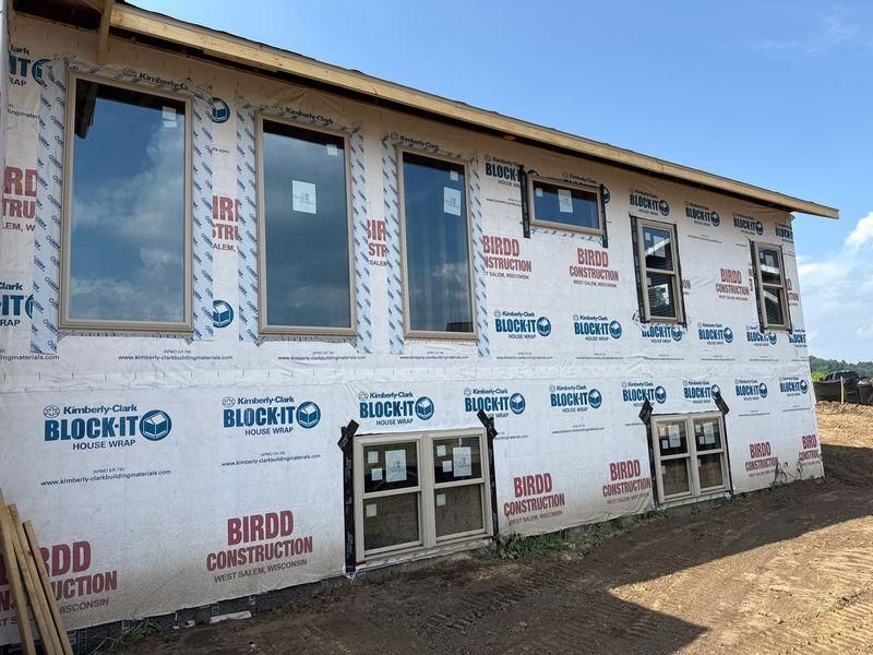 Exterior view of a residential building under construction with house wrap and newly installed windows.
