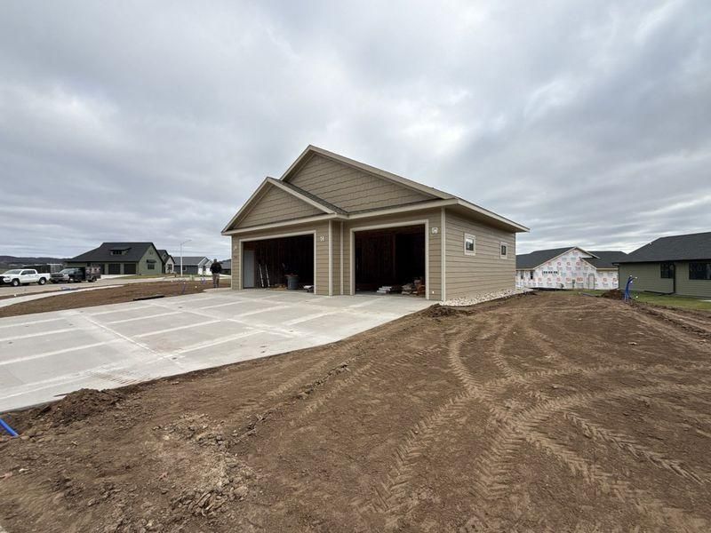 A tan, two-car garage under construction on a dirt lot with a newly poured concrete driveway.